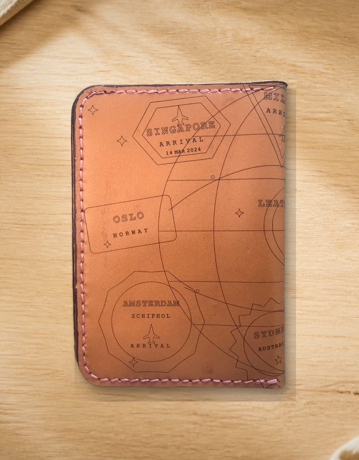 Tan leather passport holder embossed with initials, resting on a travel journal