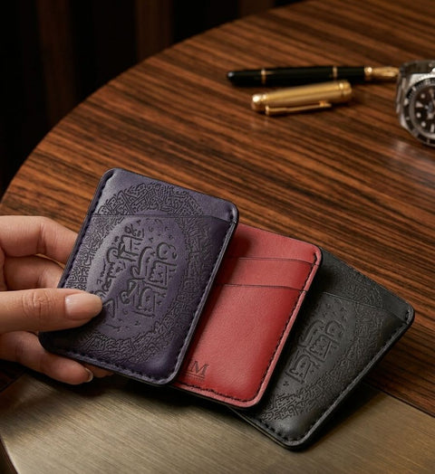 Three engraved leather card holders in plum, red and black on a wooden table